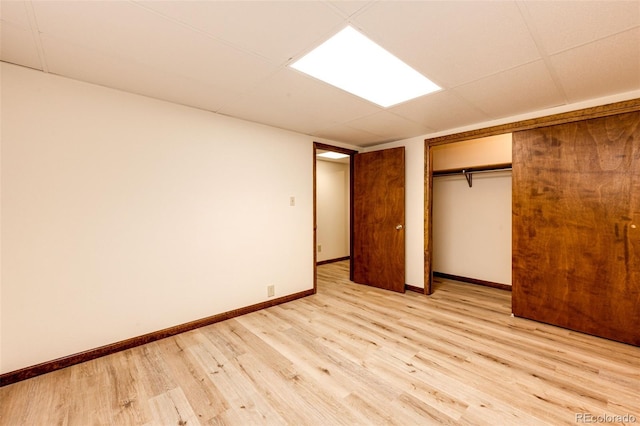 unfurnished bedroom with a paneled ceiling, a closet, and light wood-type flooring