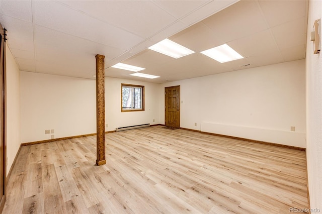 basement with a paneled ceiling, baseboard heating, and light hardwood / wood-style flooring