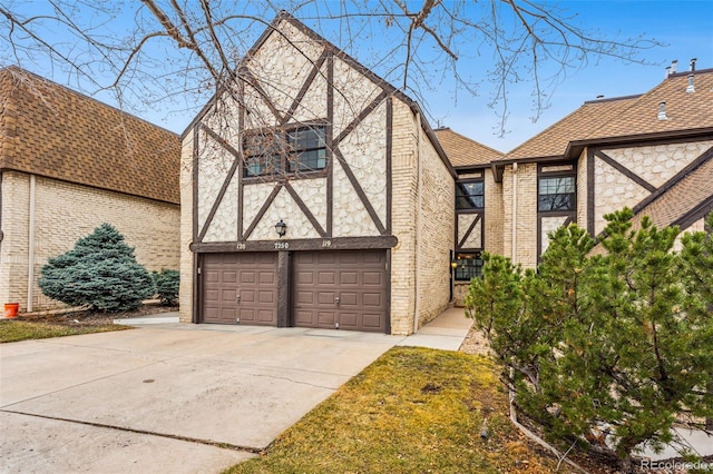 tudor home featuring brick siding, concrete driveway, an attached garage, and a shingled roof