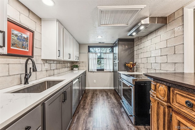 kitchen featuring a sink, backsplash, stainless steel appliances, wall chimney exhaust hood, and dark wood-style flooring