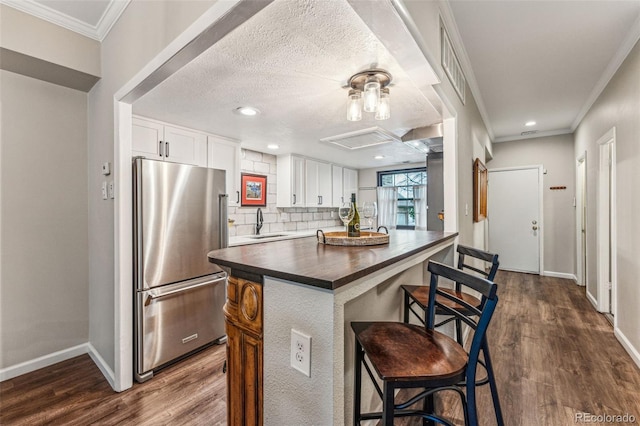 kitchen featuring a sink, freestanding refrigerator, white cabinets, decorative backsplash, and dark wood-style flooring