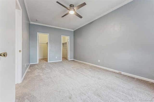 unfurnished bedroom with a ceiling fan, baseboards, carpet floors, a walk in closet, and crown molding