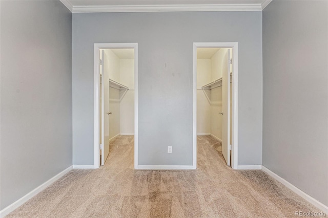 unfurnished bedroom featuring a walk in closet, a closet, crown molding, and carpet flooring