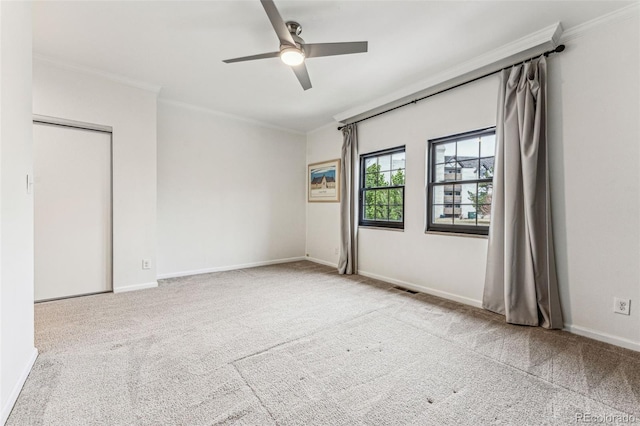 carpeted empty room featuring baseboards, ceiling fan, and crown molding