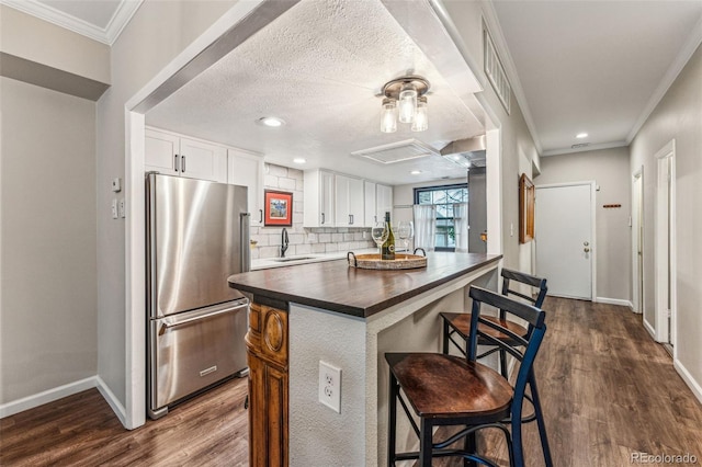 kitchen with freestanding refrigerator, ornamental molding, a sink, white cabinetry, and backsplash