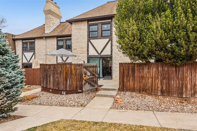 view of front of property featuring brick siding, roof with shingles, a chimney, and fence