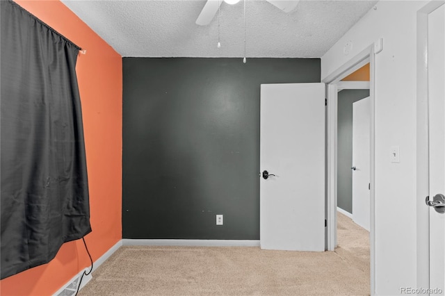 unfurnished bedroom featuring ceiling fan, light colored carpet, and a textured ceiling