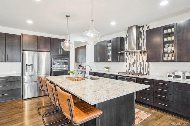 13960 Box Turtle Loop, Parker, CO 80134 - kitchen with wall chimney range hood, appliances with stainless steel finishes, a sink, dark wood finished floors, and a center island with sink