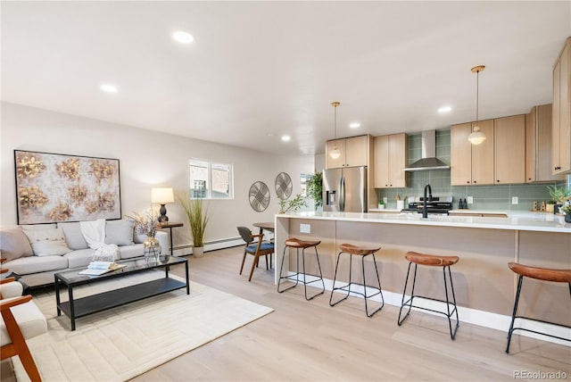 kitchen featuring hanging light fixtures, light hardwood / wood-style flooring, wall chimney exhaust hood, tasteful backsplash, and stainless steel appliances