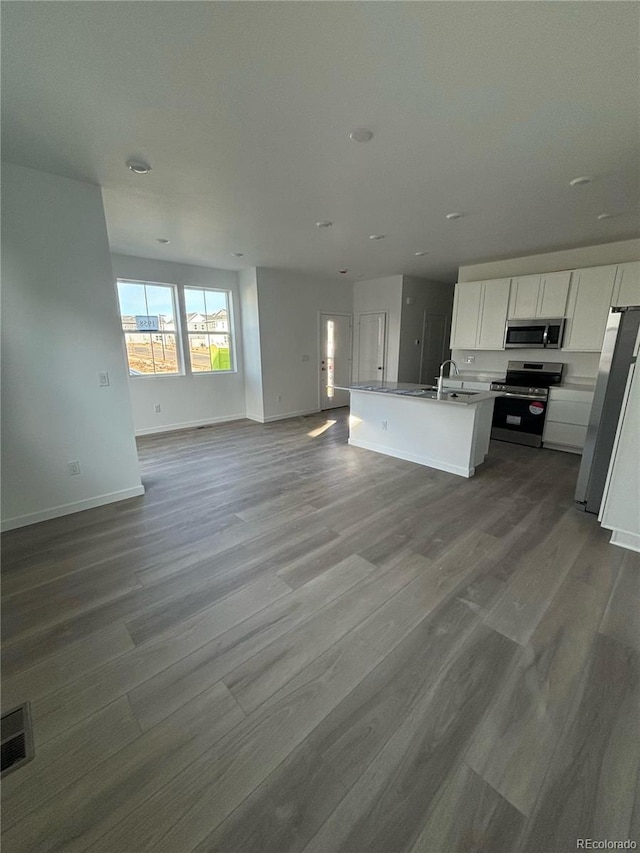 kitchen with wood-type flooring, stainless steel appliances, white cabinetry, and a kitchen island with sink