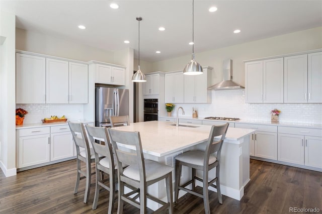 kitchen with appliances with stainless steel finishes, sink, wall chimney range hood, decorative light fixtures, and white cabinets