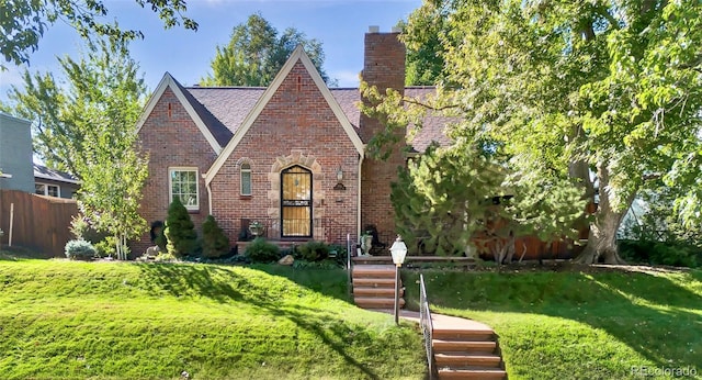 tudor home with brick siding, fence, a chimney, and a front lawn