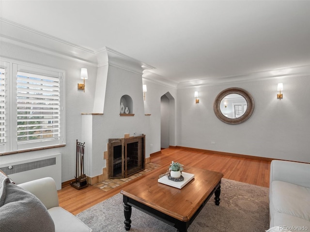 living room featuring arched walkways, crown molding, radiator heating unit, and wood finished floors