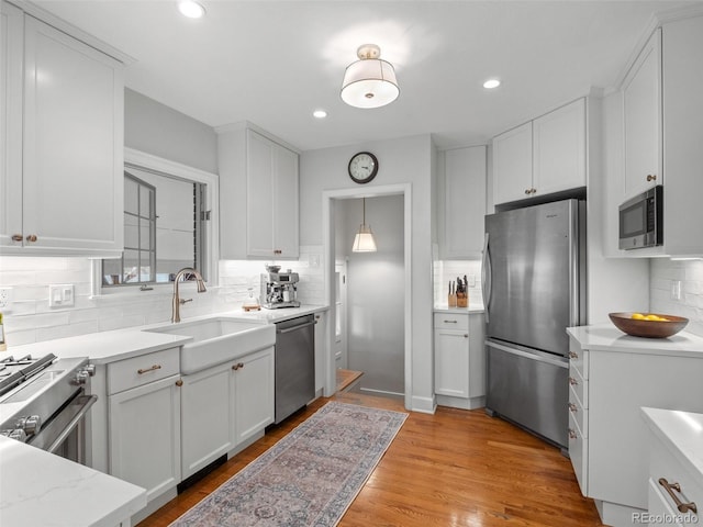 kitchen with light wood finished floors, decorative backsplash, appliances with stainless steel finishes, white cabinetry, and a sink