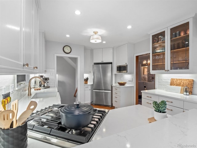 kitchen featuring glass insert cabinets, appliances with stainless steel finishes, light stone countertops, white cabinetry, and a sink