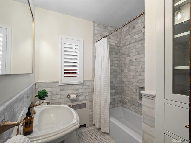 bathroom featuring a wainscoted wall, tile walls, a sink, and shower / tub combo with curtain