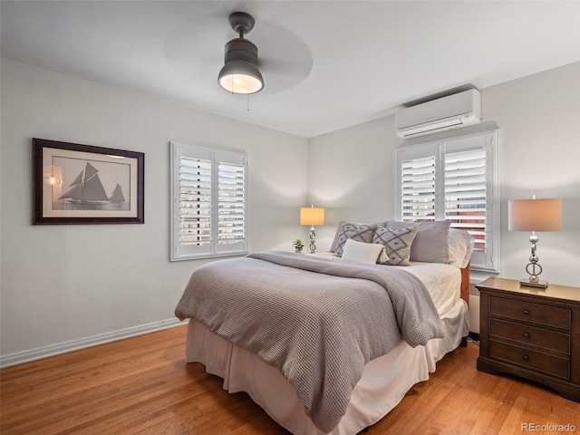 bedroom featuring a ceiling fan, a wall unit AC, baseboards, and wood finished floors