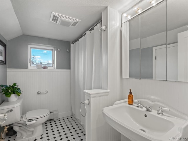 bathroom with toilet, a sink, visible vents, baseboard heating, and wainscoting