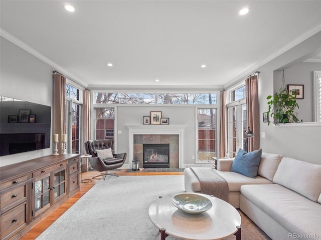 living area with light wood-style floors, a healthy amount of sunlight, crown molding, and a tiled fireplace