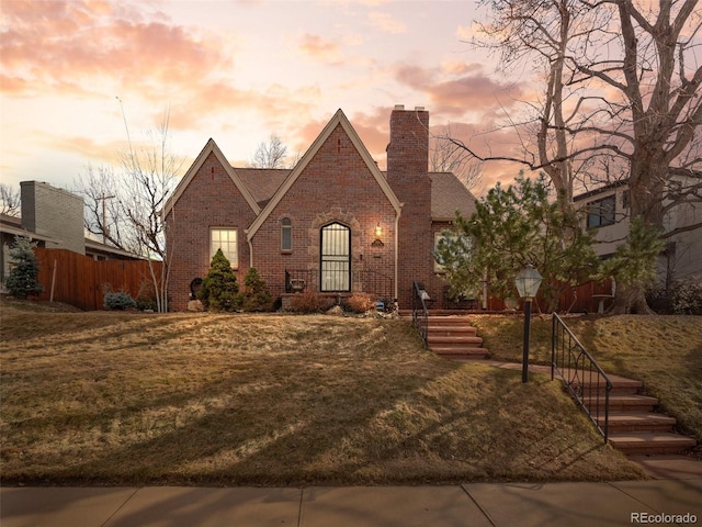 tudor home featuring brick siding, a chimney, a front yard, and fence