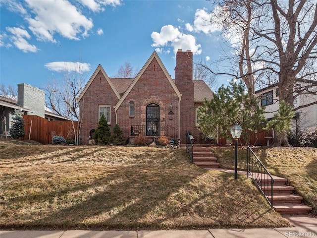 tudor house featuring brick siding, a chimney, and fence