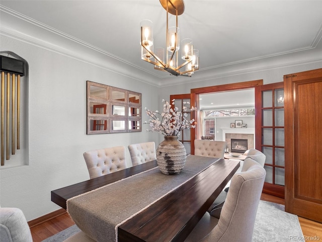 dining room with wood finished floors, crown molding, baseboards, a glass covered fireplace, and a notable chandelier
