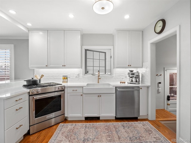 kitchen with a sink, white cabinetry, backsplash, light countertops, and appliances with stainless steel finishes