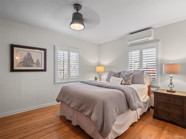 bedroom featuring ceiling fan, baseboards, wood finished floors, and a wall unit AC