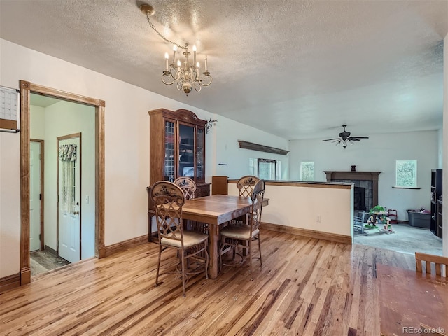 dining area with a textured ceiling, a tiled fireplace, light wood-type flooring, and ceiling fan with notable chandelier