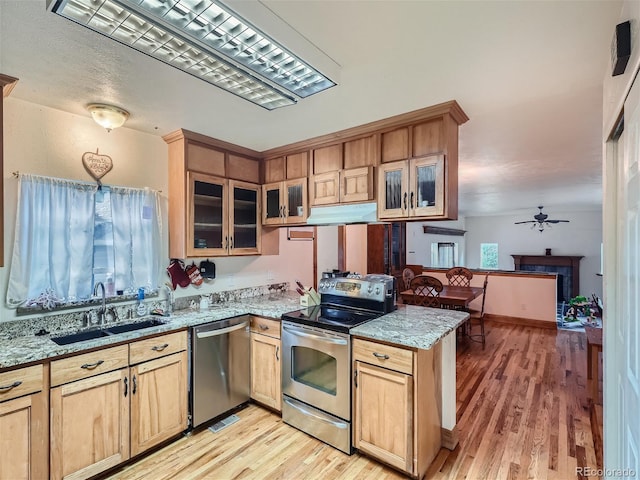 kitchen with light hardwood / wood-style floors, stainless steel appliances, kitchen peninsula, sink, and ceiling fan