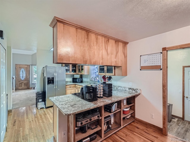 kitchen with light hardwood / wood-style floors, light stone countertops, kitchen peninsula, and stainless steel refrigerator with ice dispenser