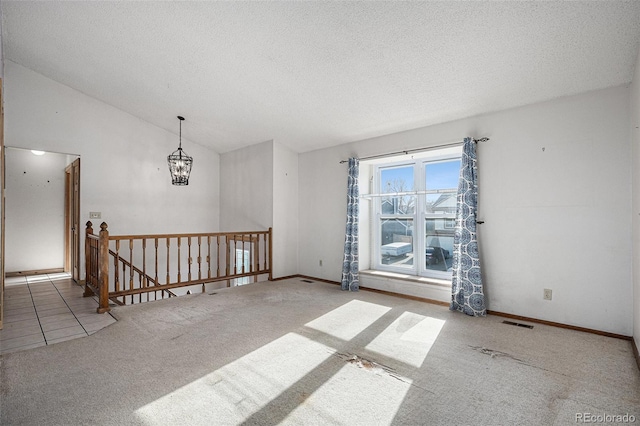 carpeted spare room featuring a textured ceiling, vaulted ceiling, and a notable chandelier