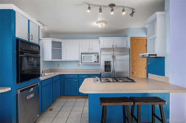 kitchen with white cabinets, light tile patterned floors, blue cabinetry, appliances with stainless steel finishes, and a kitchen bar