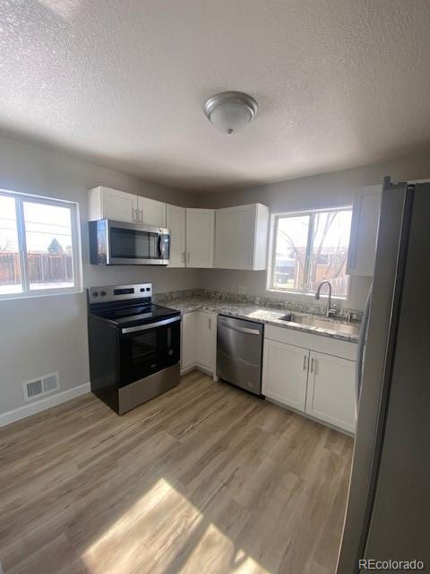 kitchen with sink, light hardwood / wood-style flooring, appliances with stainless steel finishes, white cabinetry, and a textured ceiling