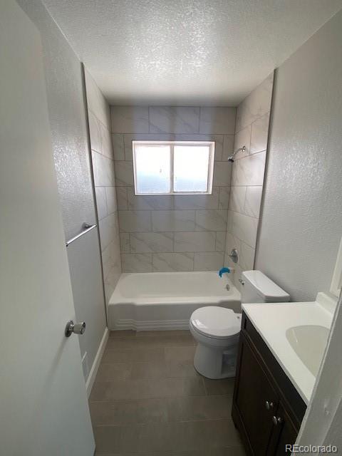 full bathroom featuring vanity, a textured ceiling, toilet, and tiled shower / bath