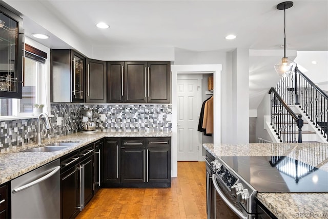 kitchen featuring decorative light fixtures, appliances with stainless steel finishes, glass insert cabinets, a sink, and light wood-type flooring