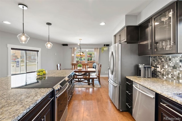 kitchen with light stone counters, stainless steel appliances, backsplash, glass insert cabinets, and dark brown cabinets