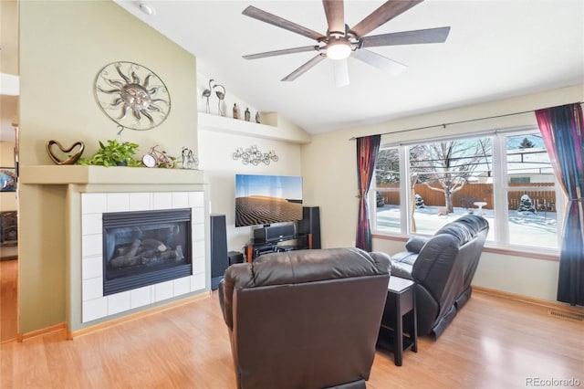 living room featuring vaulted ceiling, ceiling fan, a fireplace, and light hardwood / wood-style flooring