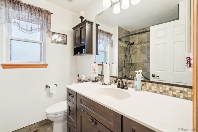 bathroom with a tile shower, vanity, and toilet