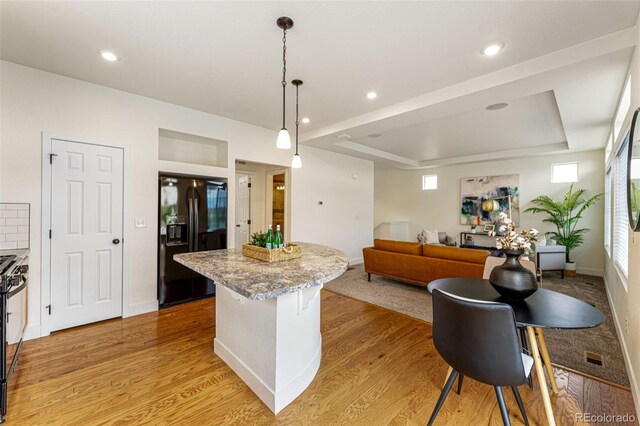 kitchen featuring light wood-type flooring, a tray ceiling, black fridge with ice dispenser, and pendant lighting