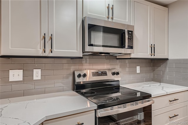 kitchen with light stone countertops, backsplash, stainless steel appliances, and white cabinets