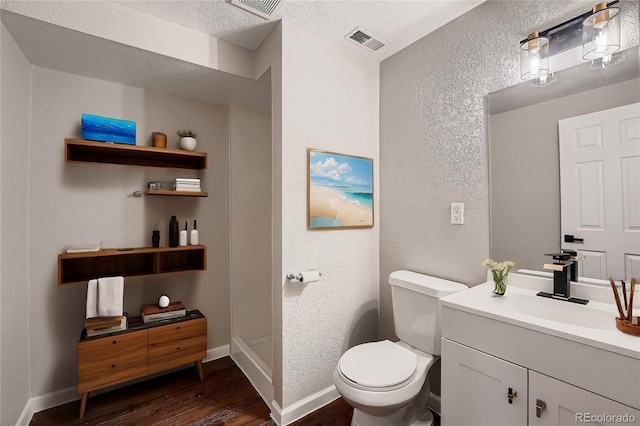 bathroom with wood-type flooring, toilet, vanity, and a textured ceiling