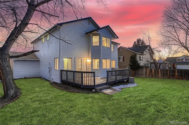 back house at dusk featuring a wooden deck and a yard