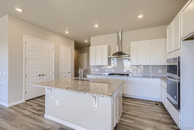 kitchen featuring white cabinetry, a kitchen island with sink, and wall chimney range hood