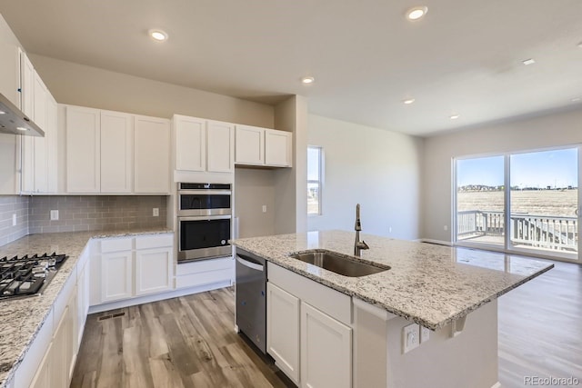 kitchen with stainless steel appliances, sink, white cabinets, light hardwood / wood-style floors, and an island with sink