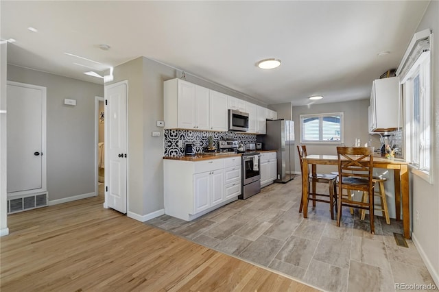 kitchen with visible vents, backsplash, appliances with stainless steel finishes, white cabinetry, and light wood-type flooring