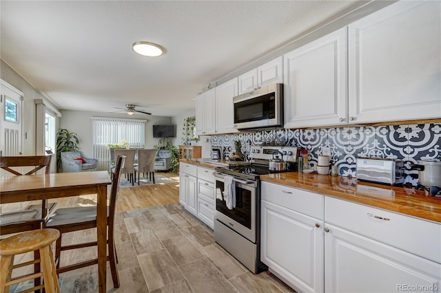 kitchen featuring decorative backsplash, a ceiling fan, butcher block counters, stainless steel appliances, and white cabinetry