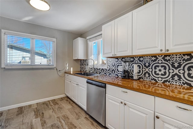 kitchen featuring baseboards, white cabinets, decorative backsplash, stainless steel dishwasher, and a sink