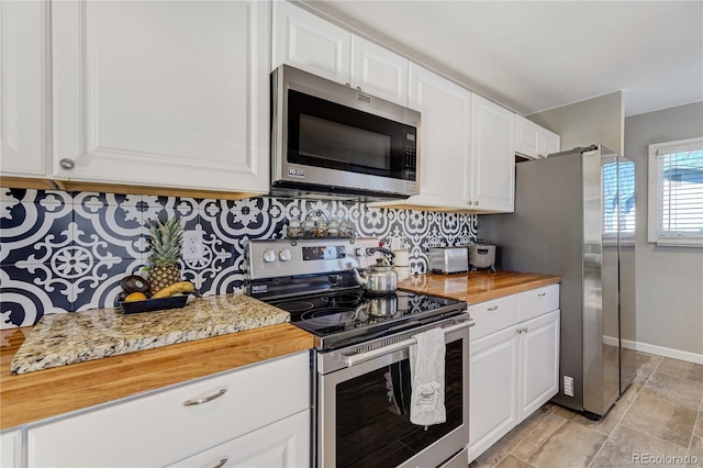 kitchen with tasteful backsplash, appliances with stainless steel finishes, white cabinets, wood counters, and baseboards