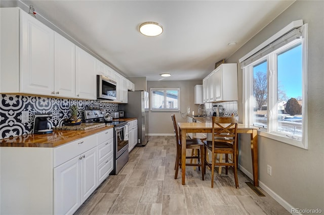 kitchen featuring stainless steel appliances, a sink, white cabinetry, baseboards, and tasteful backsplash